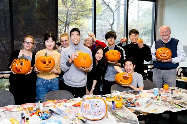 A group of international students all holding carved pumpkins smile at the camera