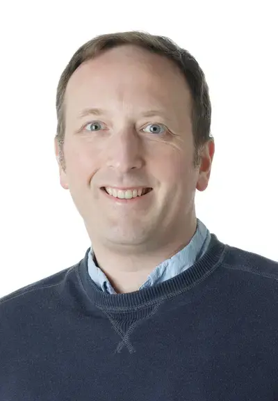 a white man in a blue sweater smiling at the camera