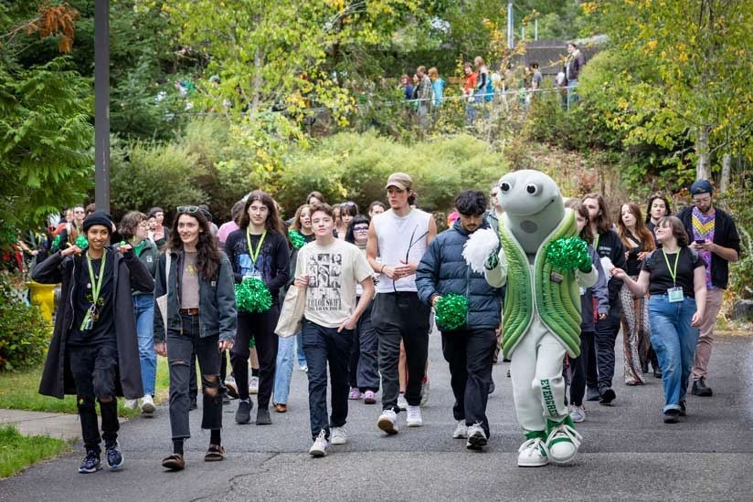 a group of students and geoduck mascot character walking together in a woodland area