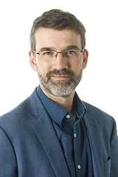 Portrait of Noah Coburn wearing dark blue jacket and matching shirt