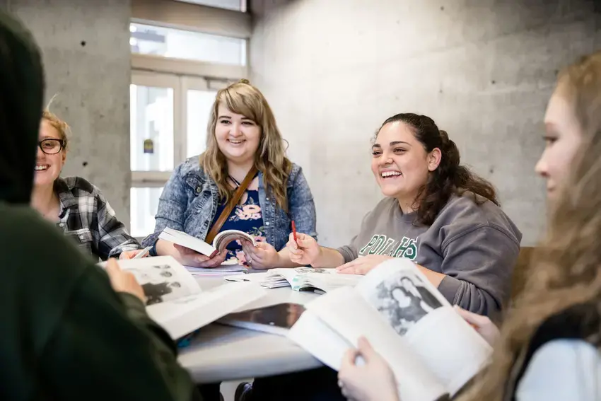 students around a table holding books and talking 