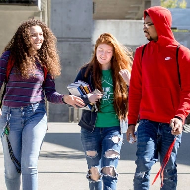 three students walking and talking on a campus sidewalk